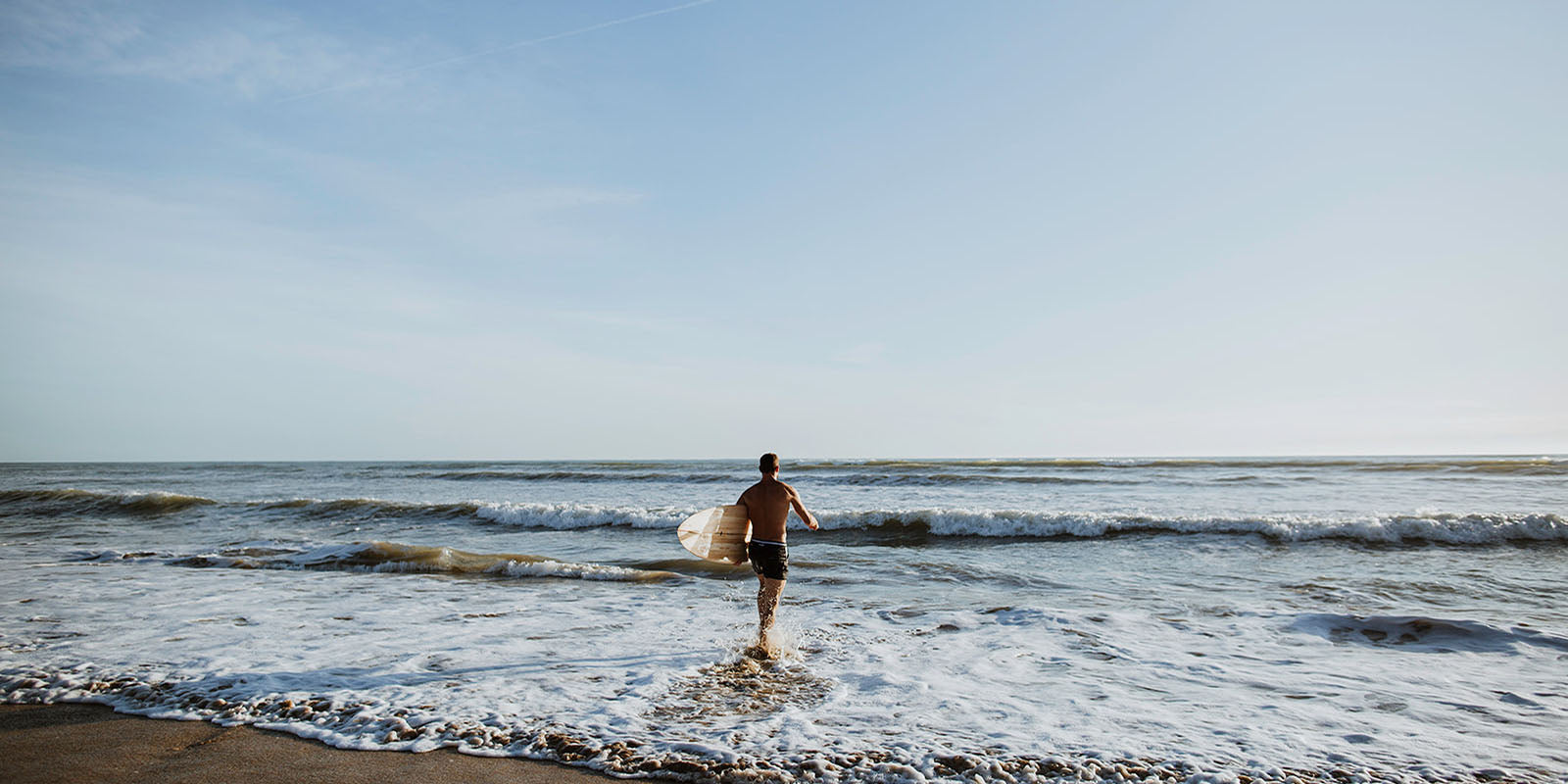 BLUEBUCK-surfer-with-recycled-swim-shorts-on-beach-into-water